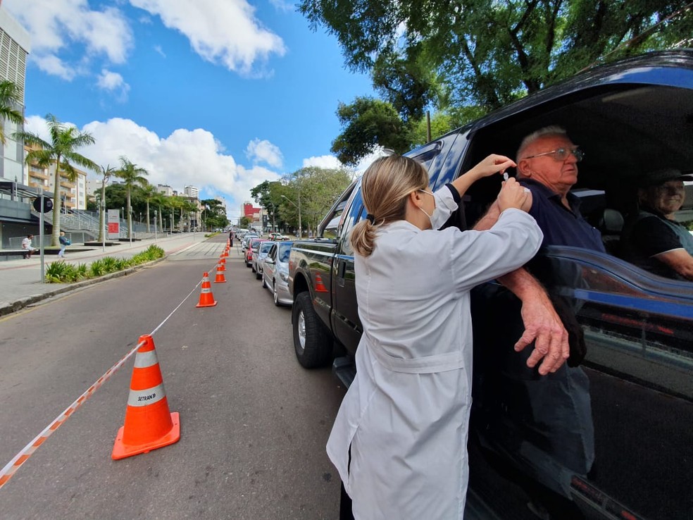 Notícia: A 1ª fase da campanha de vacinação contra a gripe começa hoje em Curitiba. Na foto, um idoso sendo vacinado na campanha contra a gripe. Cores na imagem: preto, branco, laranja e azul. 
