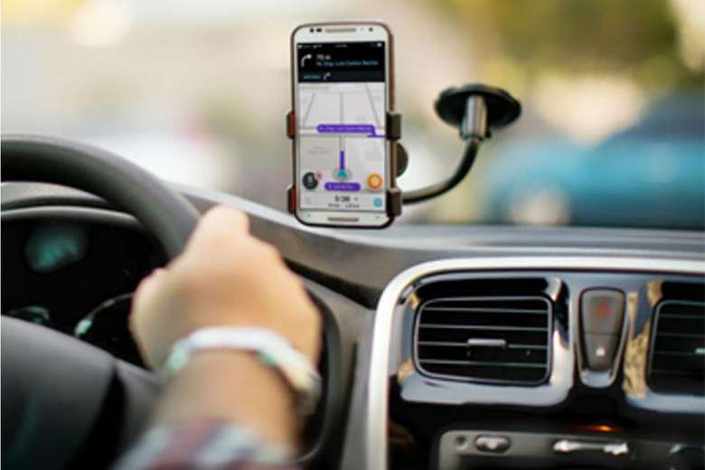 notícia: Uber fará corridas de graça para quem for doar sangue. #PraCegoVer: na foto, um celular apoiado dentro do carro com o aplicativo de GPS Waze aberto. Cores na imagem: preto, verelho, laranja, roxo, branco, azul.