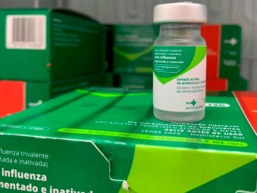 notícia: Terceira fase da vacinação contra a gripe começa na segunda-feira (11) em Curitiba; veja onde receber a dose. #pratodosverem: frasco da vacina contra H1N1 em cima de uma caixa. Cores na imagem: verde, branco, vermelho e cinza. 